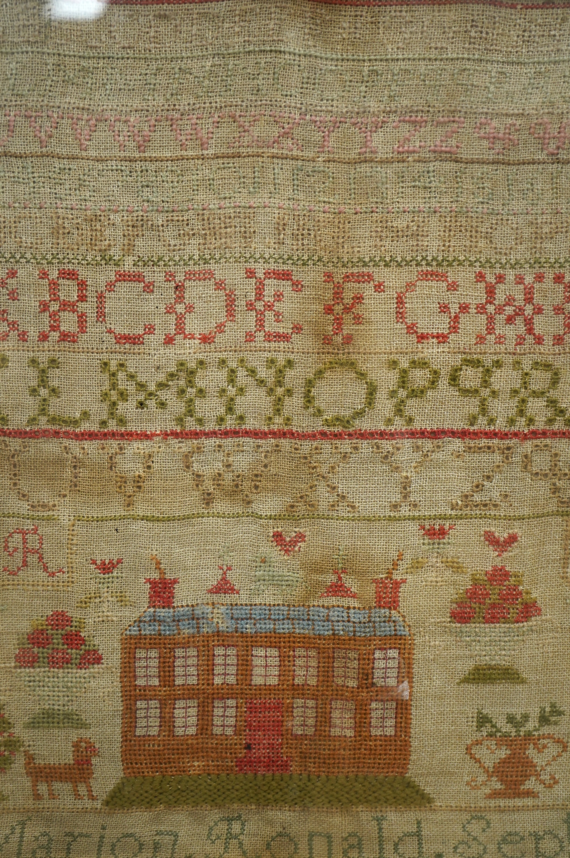 A 19th century sampler by Marion Ronald dated 1846, worked with various alphabets in cross stitch and buttonhole stitch, the lower section depicting a large thirteen windowed house surrounded by various spot motifs, a do